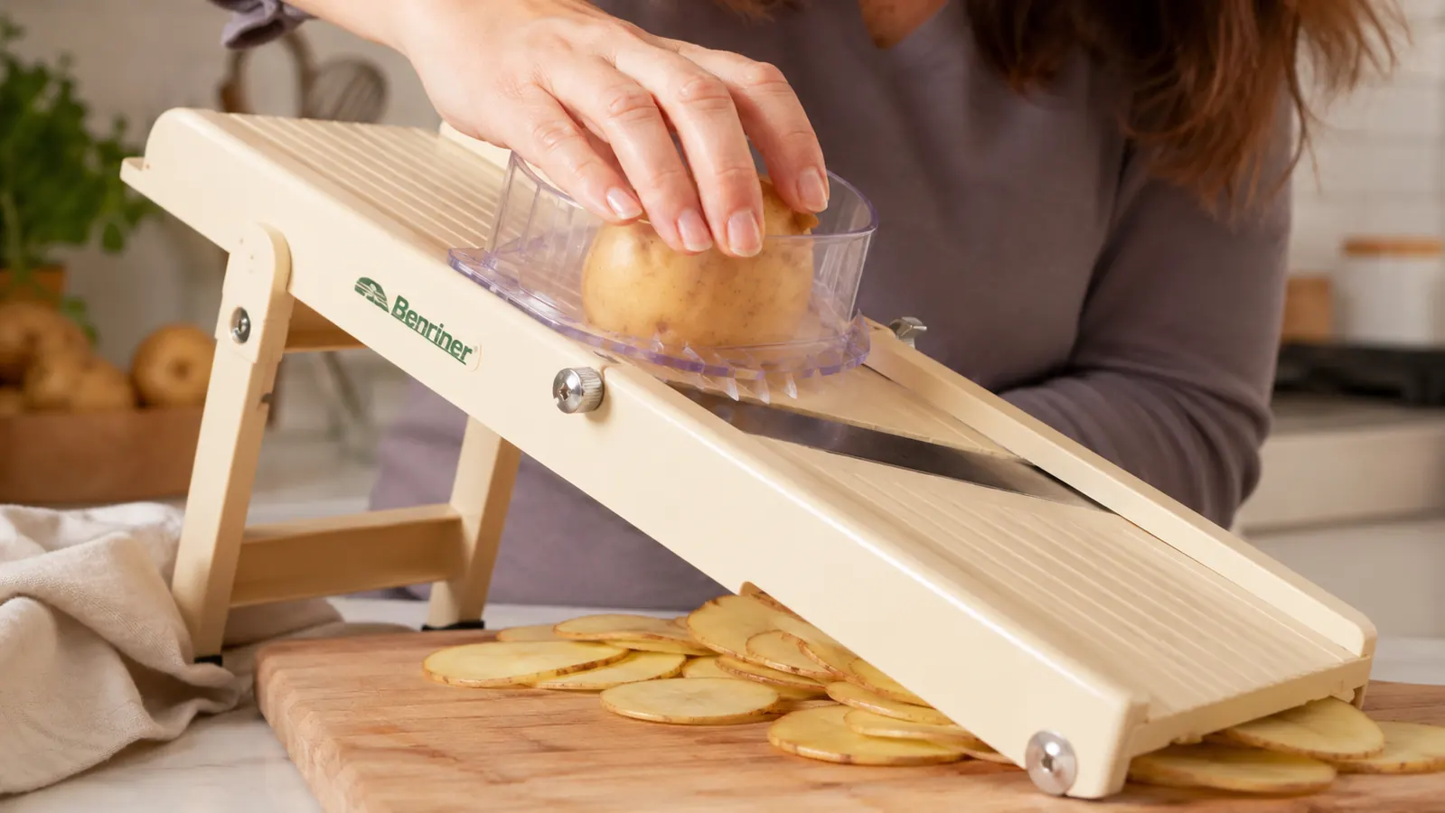 Hand using the food holder to guide a potato across a mandoline slicer's blade