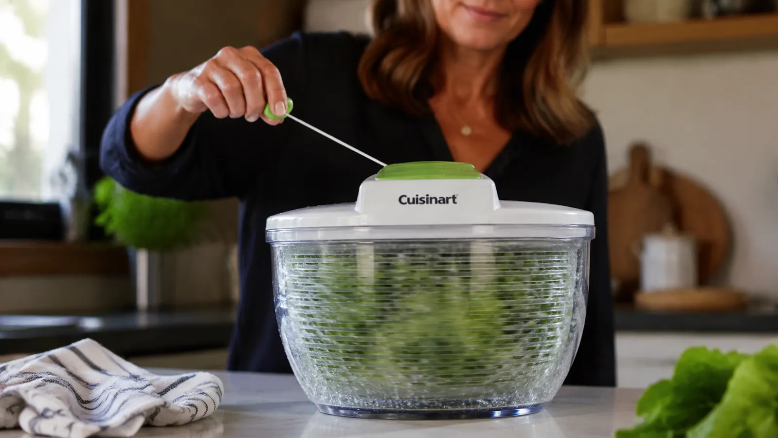 Hand pulling the cord on top of a Cuisinart salad spinner with wet lettuce visible spinning inside the clear bowl
