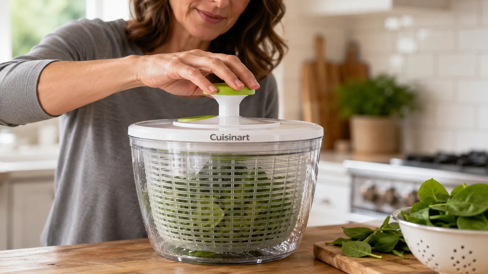 Hand pulling the pump-style top of the Cuisinart salad spinner to spin dry a basket of spinach