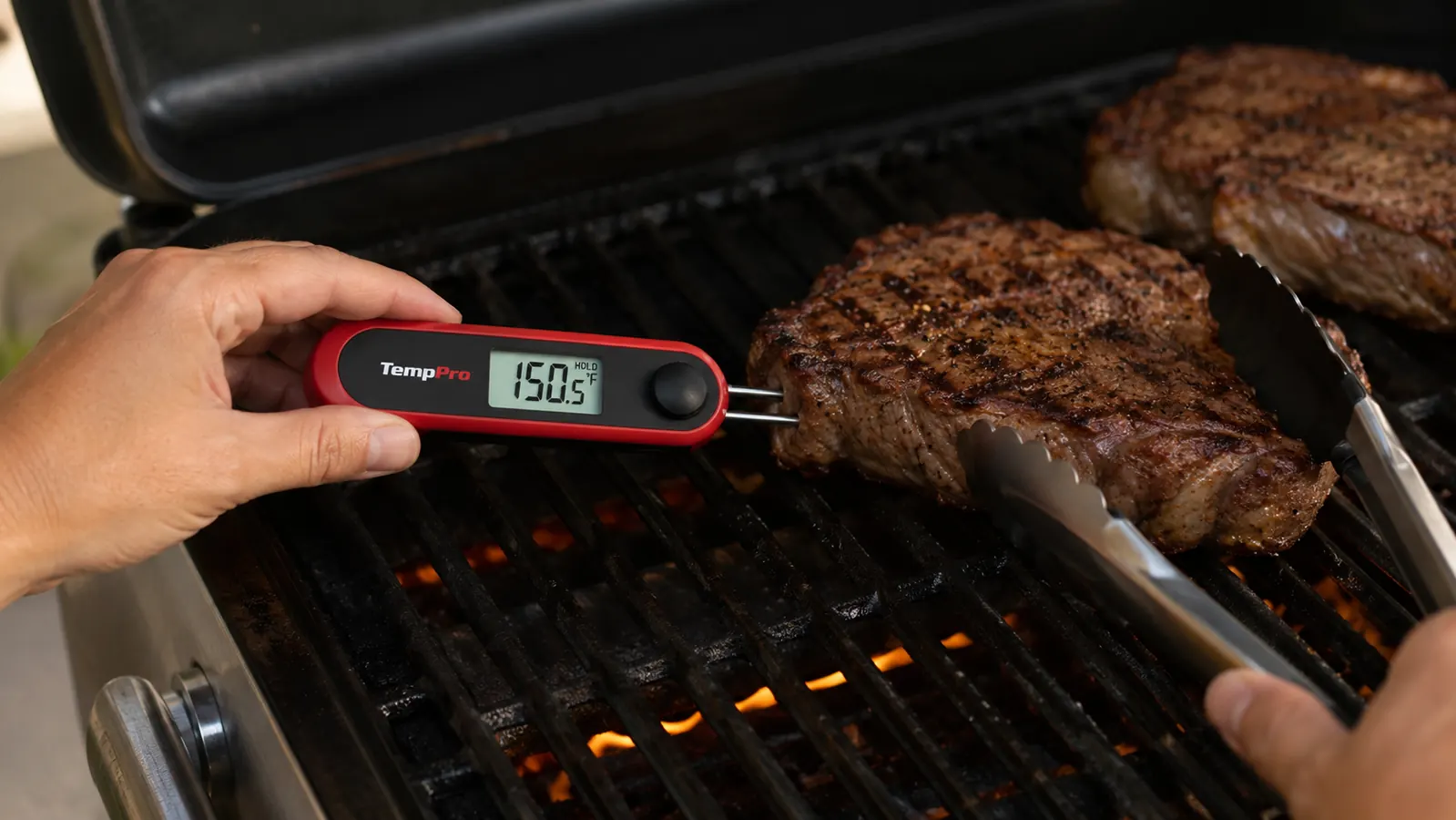 A hand inserting the TempPro TP17 thermometer probe sideways into the thickest part of a steak on the grill grates